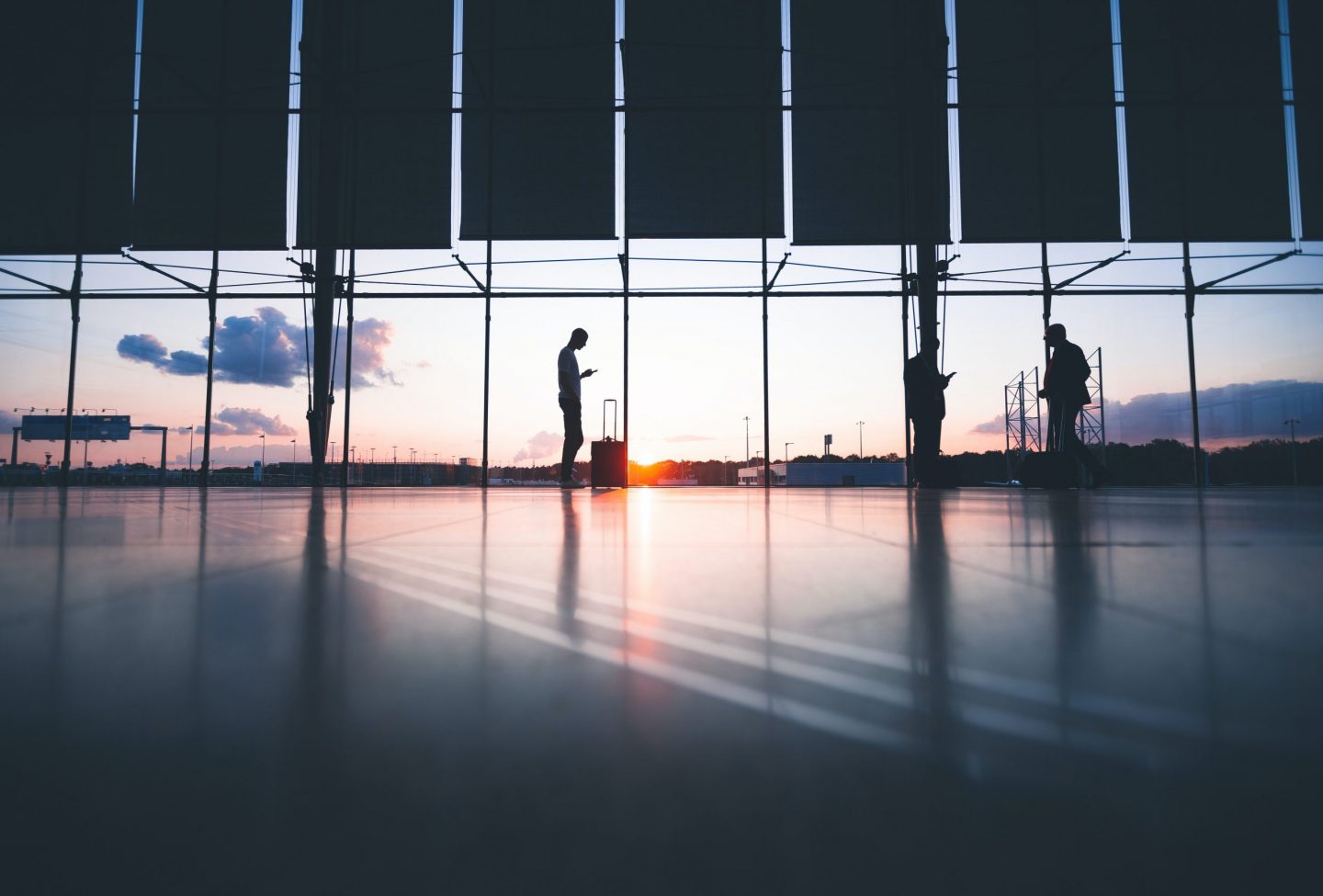 Two man stand apart in front of airport window
